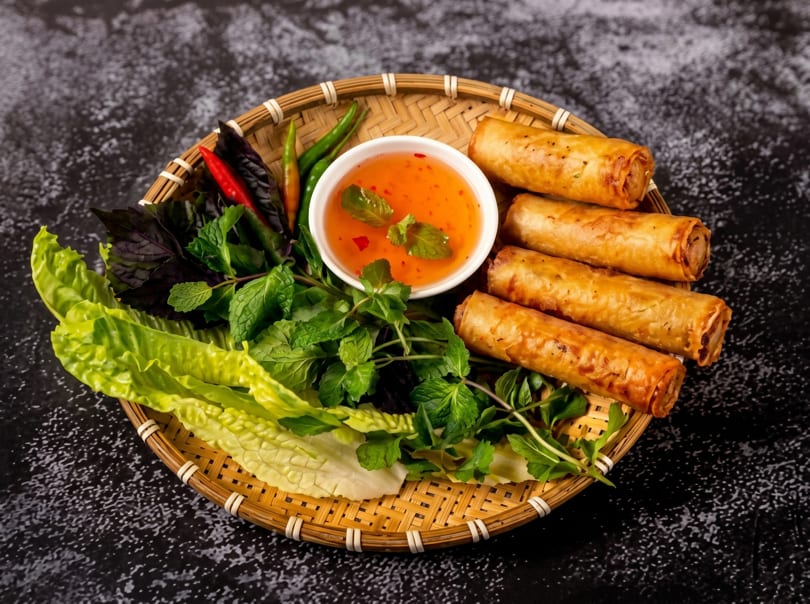 Crispy Vietnamese spring rolls, fresh herbs, and dipping sauce arranged on a woven tray.