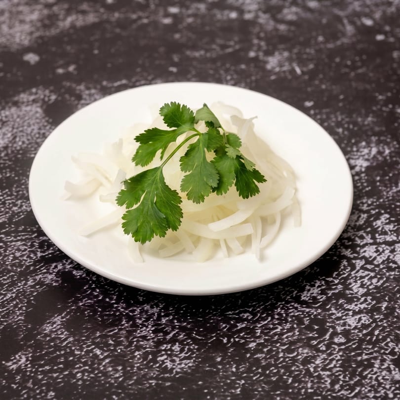 A white plate holds thinly sliced white onions garnished with fresh green cilantro.